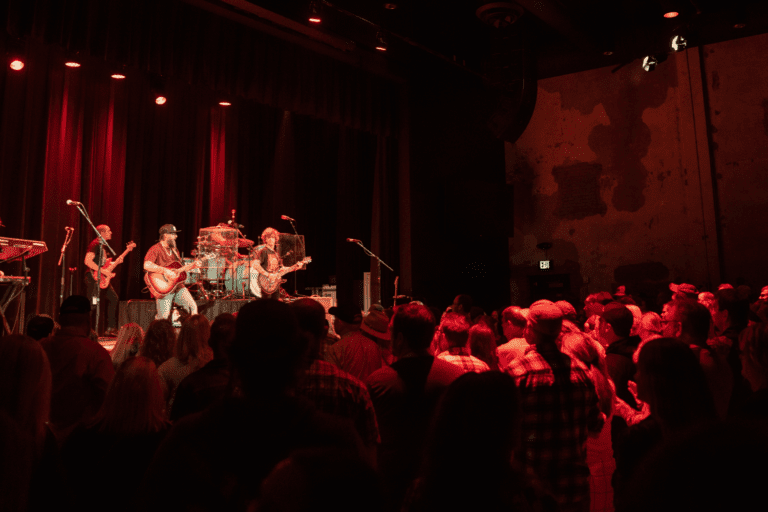 Musicians on stage with audience in dark theater.